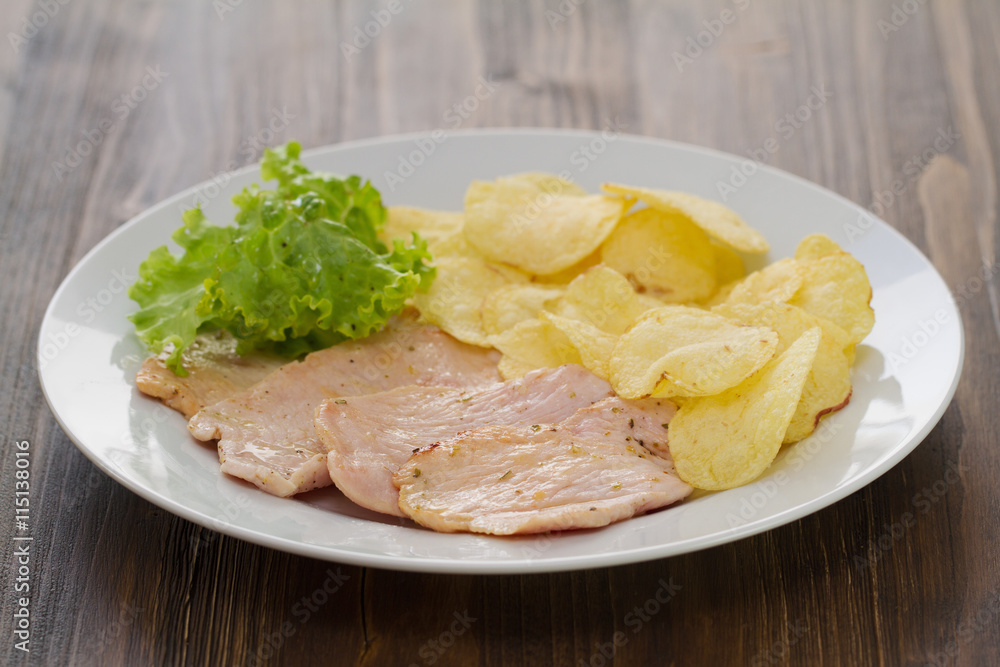 fried meat with potato chips and fresh lettuce on white dish