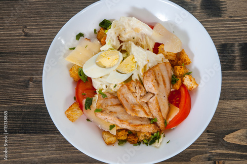 Caesar salad with croutons, cheese, eggs, tomatoes and grilled chicken on wooden table