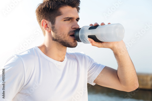 Sportsman in white shirt drinking water outdoors