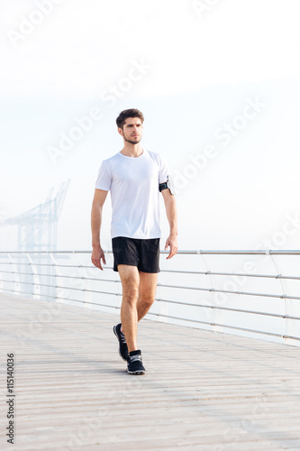 Attractive young sportsman walking on pier