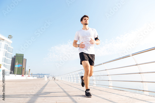 Concentrated young sportsman running on pier in the morning
