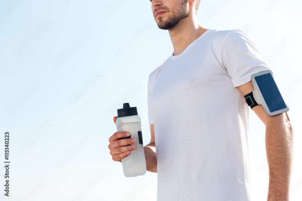 Cropped image of a male sportsman holding water bottle outdoors Cropped image of a male sportsman holding water bottle outdoors