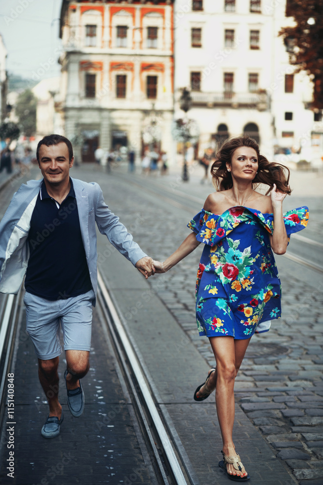 Man in blue shorts run along the street with a lady in flowered