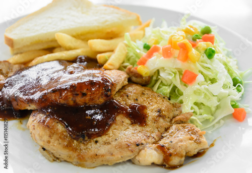 Grilled pork steak fillet with salad and French fries on white plate