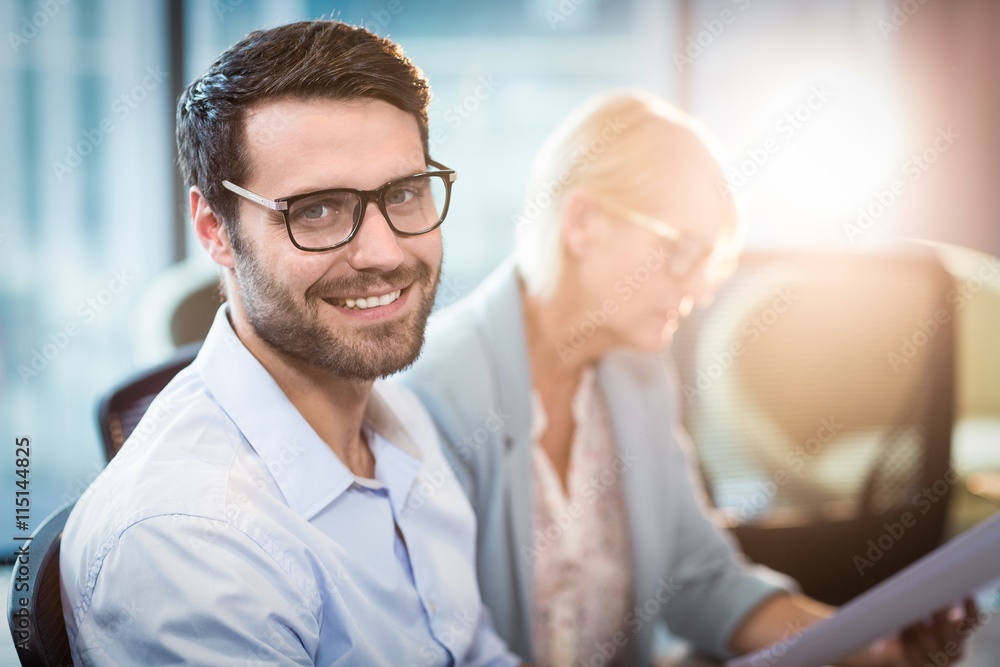 Obraz premium Man smiling at camera while his colleague reading document