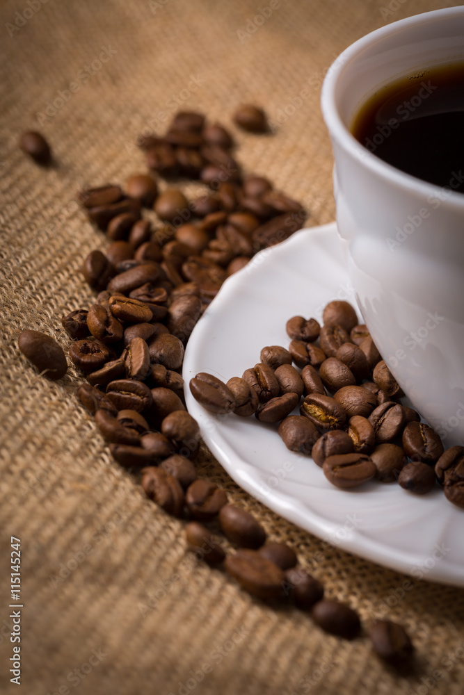 Tasse Kaffee mit Untertasse und Kaffeebohnen auf Leinentuch, Nah Tasse Kaffee mit Untertasse und Kaffeebohnen auf Leinentuch, Nah