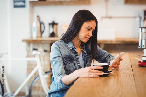 woman text on phone while holding coffee 