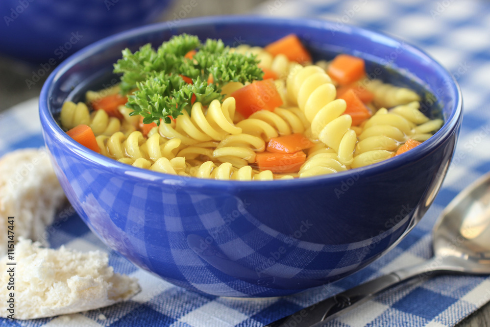 chicken soup with pasta, carrots and parsley in a blue bowl