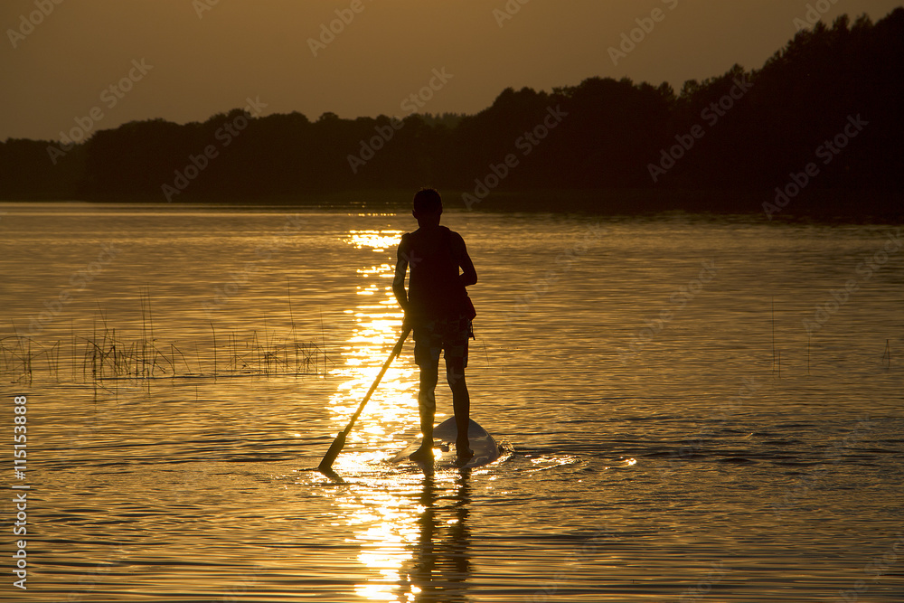 Silhouette boy on sup-board stand up paddle board in late evening during sunset