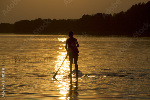 Silhouette boy on sup-board stand up paddle board in late evening during sunset