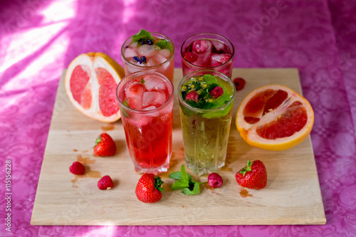 Four homemade refreshing summer cocktails and drinks with ice fresh berries, strawberry, raspberry and grapefruit on wooden cutting Board 