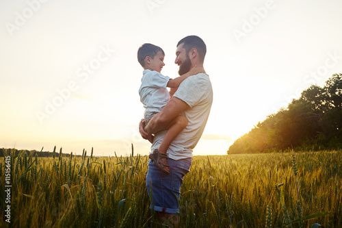 Father holding small son in field during beautiful sunset