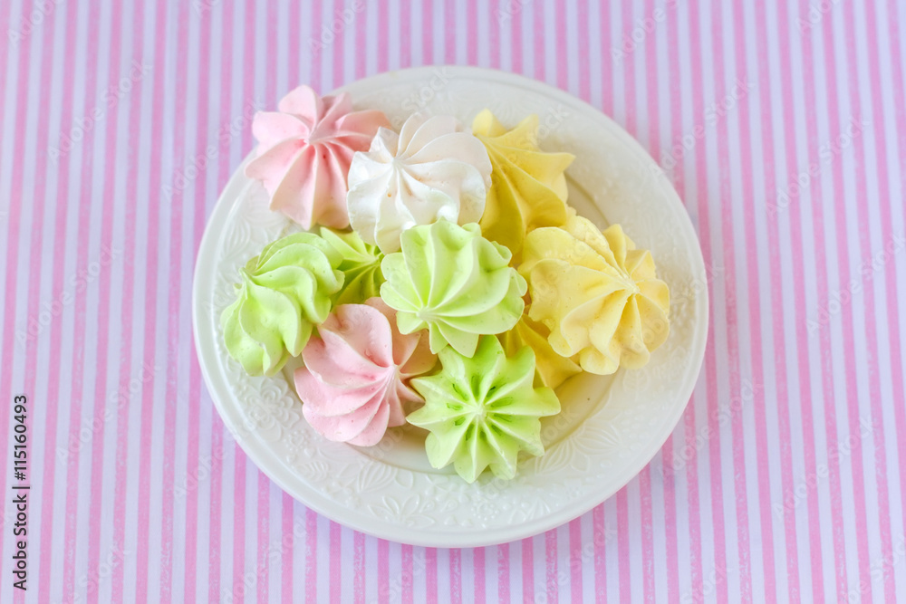 Multi-colored meringue on a white saucer on the background of the tablecloth