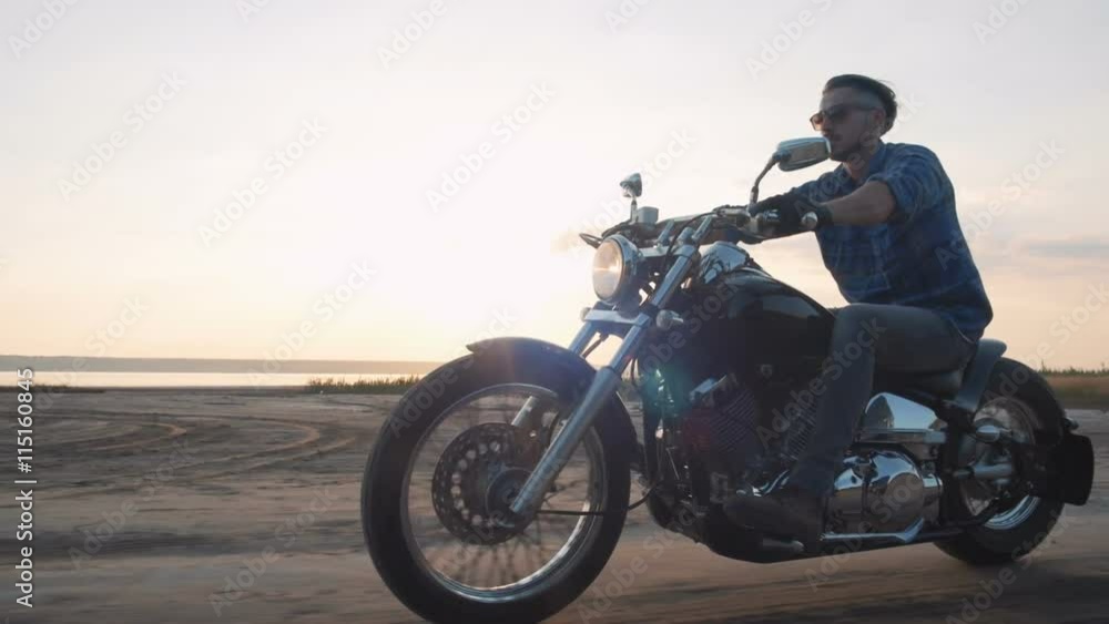 Motorcyclist driving his motorbike on the road during sunset near the water Motorcyclist driving his motorbike on the road during sunset near the water