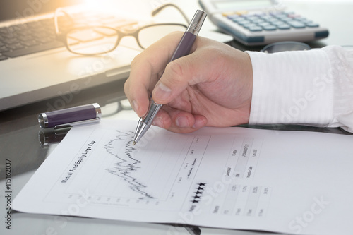 Businessman or fund manager review Mutual Fund information with performance line graph and benchmark with pen calculator and computer laptop.