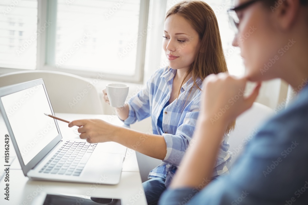 Businesswoman pointing on laptop with colleague in office Businesswoman pointing on laptop with colleague in office