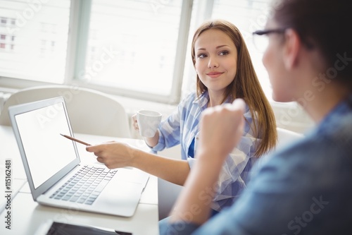 Happy businesswoman pointing on laptop with colleague in office