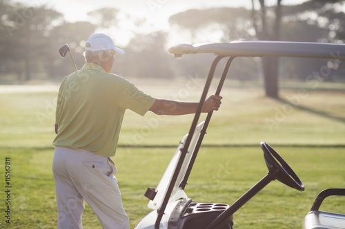 Rear view of mature man standing by golf buggy 