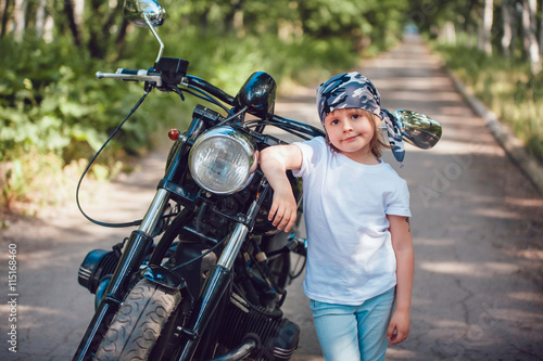 Little girl in a white T-shirt and bandana standing near  motorcycle © kanashkin