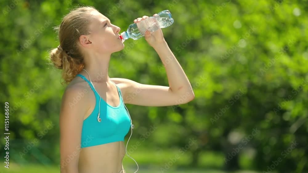 Slim young woman drinking water after training. Woman athlete takes a break, she drinking water, out on a run on a hot day. Slim young woman drinking water after training. Woman athlete takes a break, she drinking water, out on a run on a hot day.