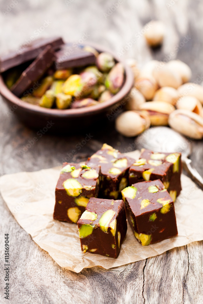 Fototapeta premium Dark chocolate cubes with pistachios on wooden background