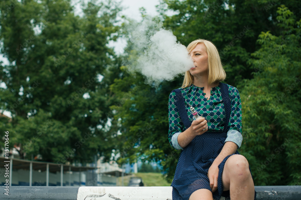 girl sitting on a concrete block smokes electronic cigarette vaporizes steam girl sitting on a concrete block smokes electronic cigarette vaporizes steam