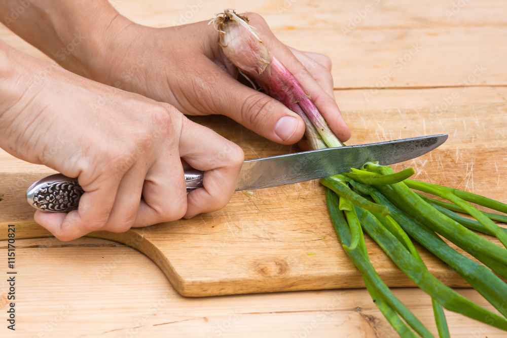 hands chopping green onion on the wooden cutting board