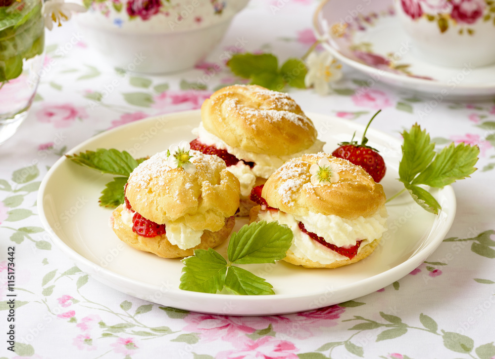 Cream puffs cakes or profiterole filled with whipped cream and served with strawberries on the table Cream puffs cakes or profiterole filled with whipped cream and served with strawberries on the table