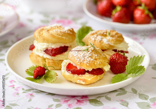 Cream puffs cakes or profiterole filled with whipped cream and served with strawberries on the table