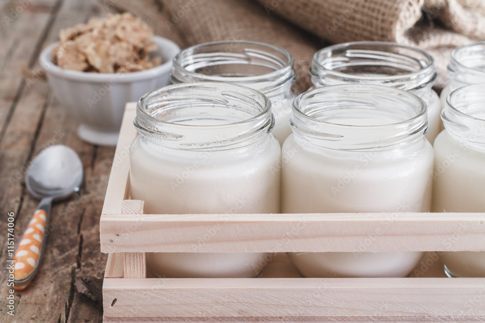 Yogurt in jars homemade in a wooden box. Bowl of cereal in the background. Yogurt in jars homemade in a wooden box. Bowl of cereal in the background.