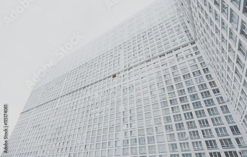 Huge contemporary white and grey residential skyscraper apartment building with multiple regular windows on facade  Moscow  bright cloudy day  view from bottom