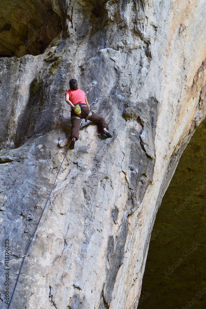 Young woman rock climber high on a vertical rocky wall in Prohodna Cave, Bulgaria
