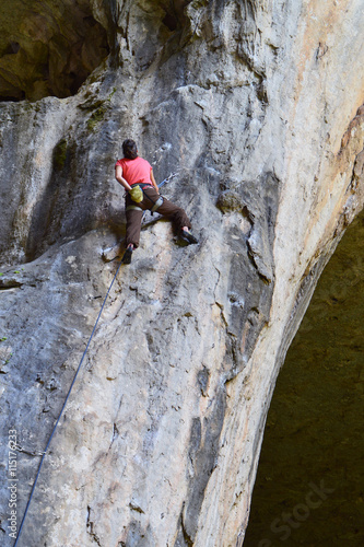 Young woman rock climber high on a vertical rocky wall in Prohodna Cave, Bulgaria