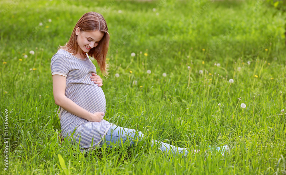 Fototapeta premium Beautiful pregnant woman sitting on grass