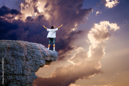 Man standing on cliff above cloudy sky