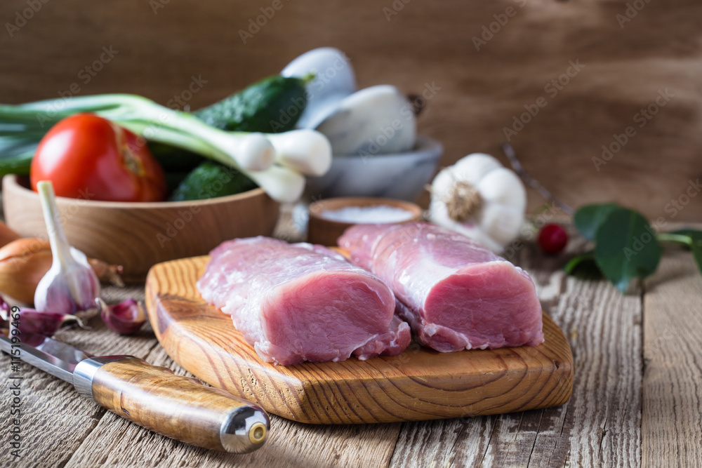 Raw pork tenderloin and vegetables on rustic wooden table Raw pork tenderloin and vegetables on rustic wooden table