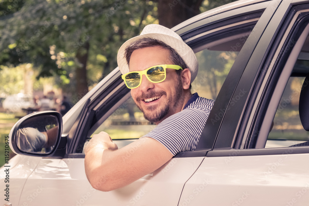 Naklejka premium Portrait of young driver wearing sunglasses in driver’s seat. Vacation and travel concepts.
