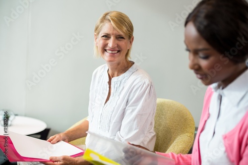 Woman smiling at camera while her colleague reading document