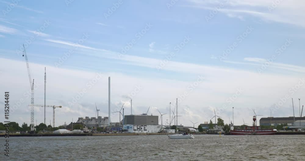 Boat sailing along the shore in the city. Harbour and industrial city district with working windmills Boat sailing along the shore in the city. Harbour and industrial city district with working windmills