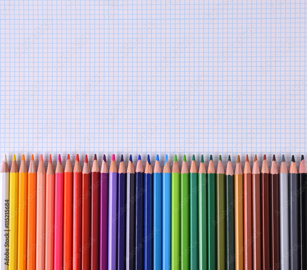Colored pencils lined up palette on checkered white sheet Colored pencils lined up palette on checkered white sheet