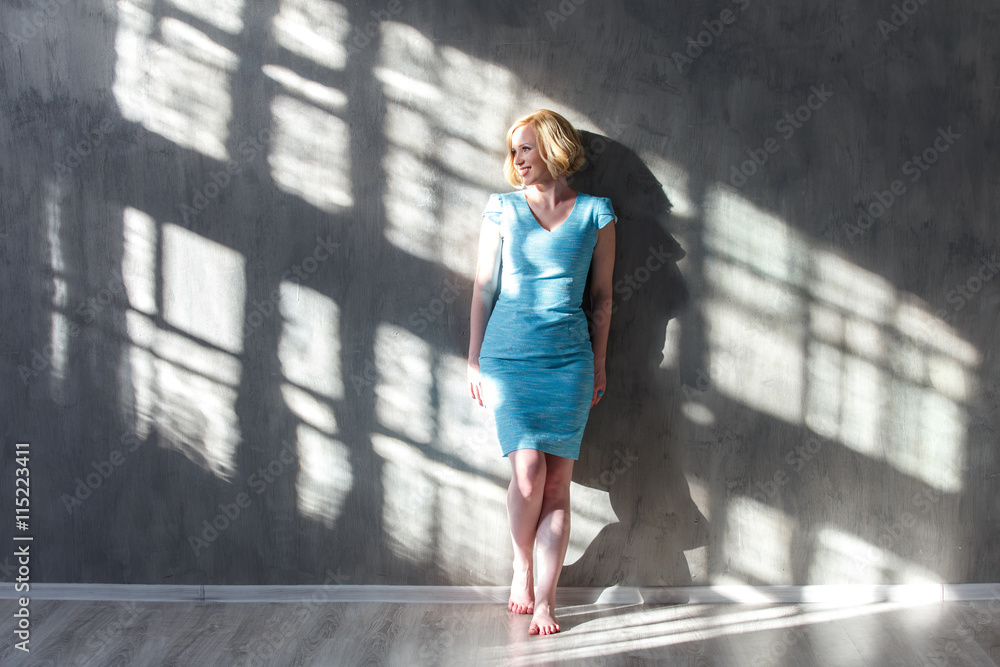 Smiling blond woman leaning on the wall and looking on sunlight