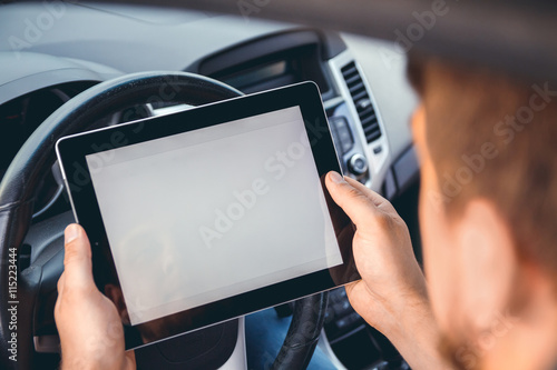 A young man with a tablet in his hand at the wheel of the car. Multitasking. Safe driving concep photo