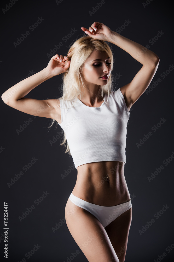 Fototapeta premium Fashion photo of beautiful blonde fit woman with magnificent hair posing on grey studio background