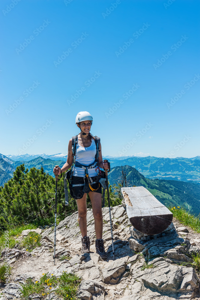 Single woman with hiking sticks near log bench