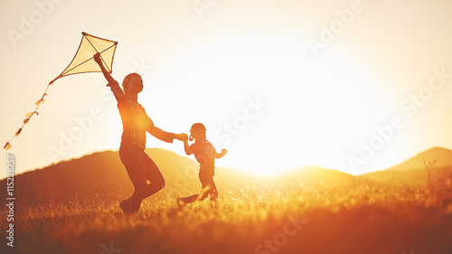 happy family mother and child run on meadow with a kite in the s photo