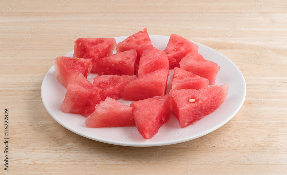 Small sections of watermelon on a plate atop a wood table.