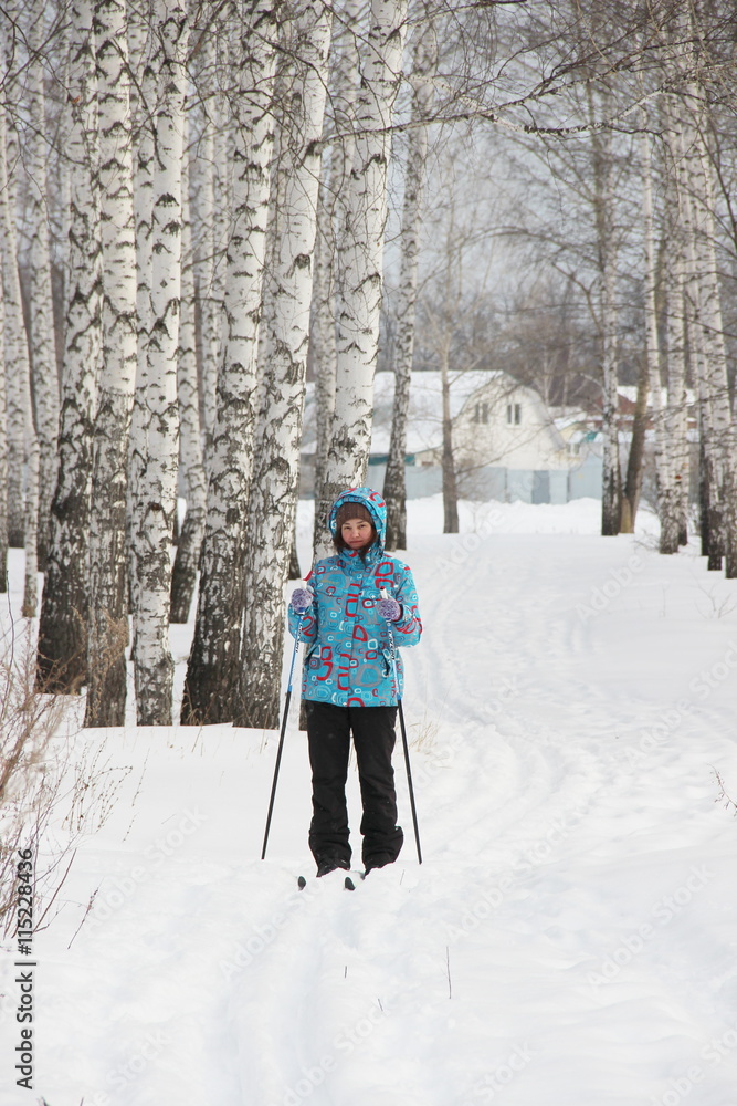 a girl in a blue jacket is skiing in the winter snowy forest