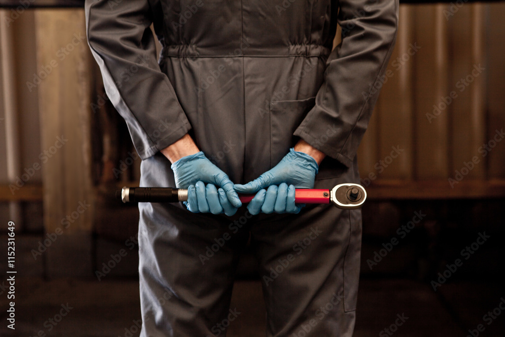 Male mechanic holding socket wrench behind back, rear view, mid section Male mechanic holding socket wrench behind back, rear view, mid section