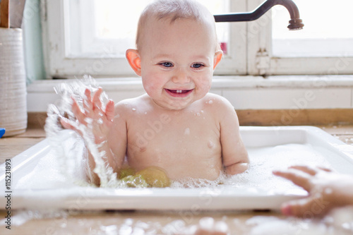 Baby boy splashing whilst bathing in kitchen sink photo