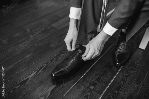 Business man dressing up with classic, elegant shoes. Groom wearing shoes on wedding day, tying the laces and preparing. Black and white photo